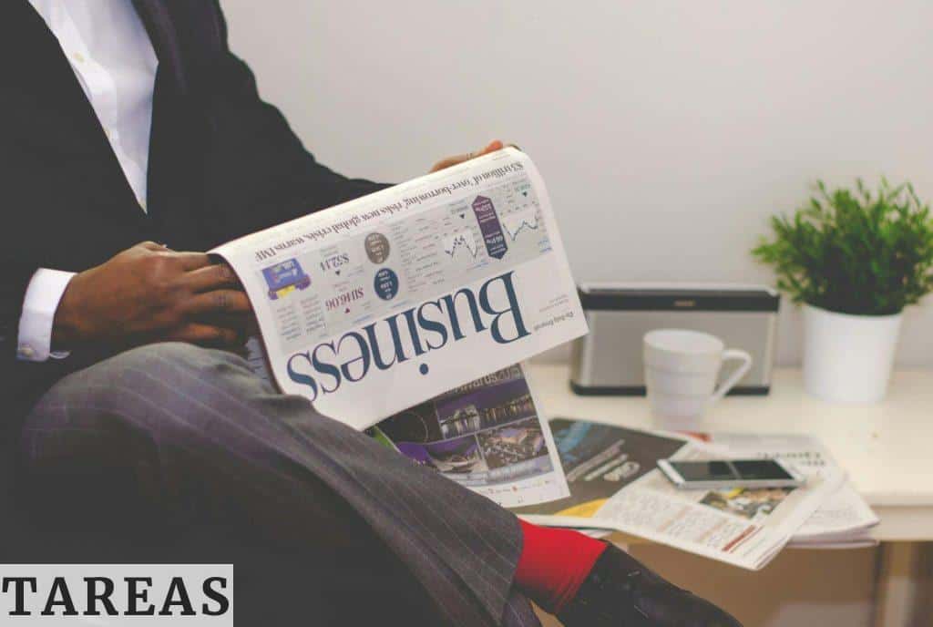 Man Reading Newspaper While Sitting Near Table With Smartphone and Cup