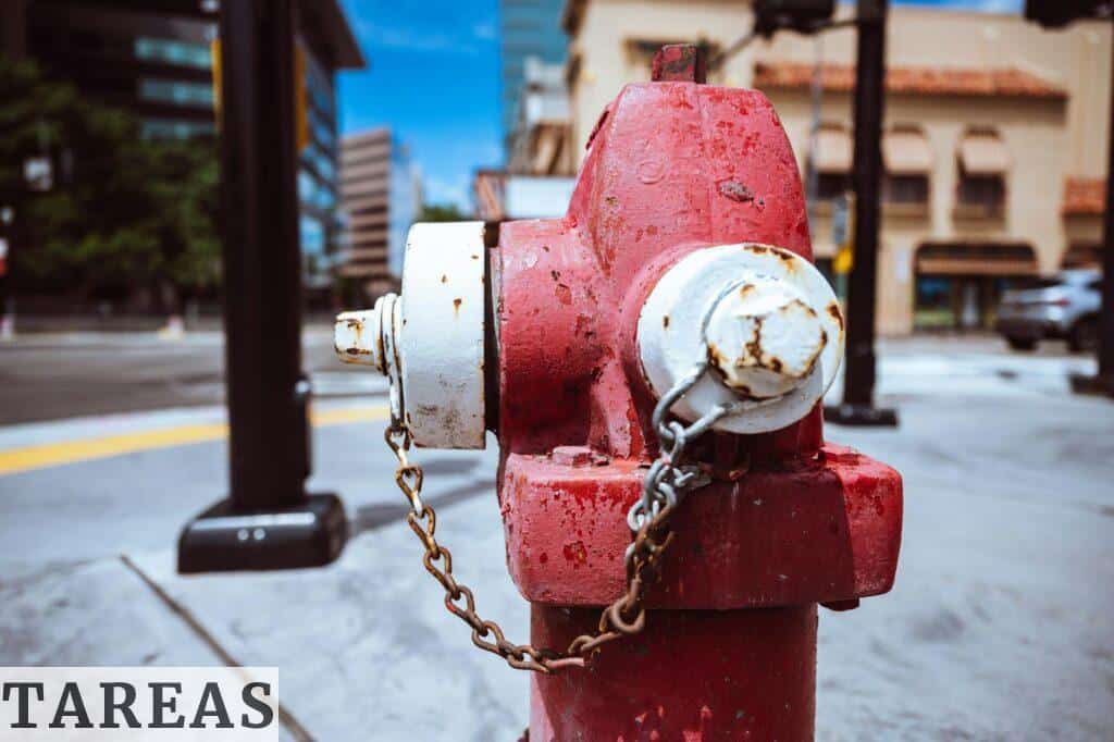 Typical red fire hydrant with rusty chain located on roadside in modern city on sunny day