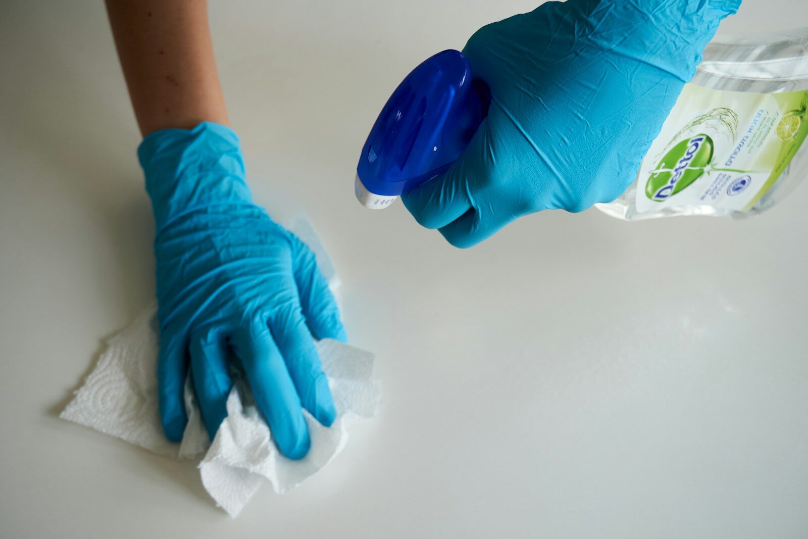 Manos con guantes limpiando una superficie durante la limpieza del hogar
